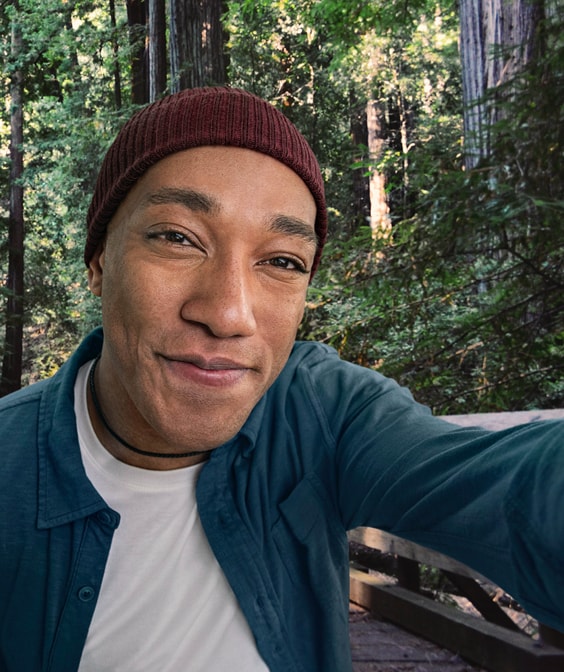 Mixed ethnicity male in hat taking a selfie in front of a wooded forest, not actual Serostim® patient