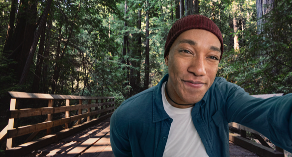 Mixed ethnicity male in hat taking a selfie in front of a wooded forest, not actual Serostim® patient