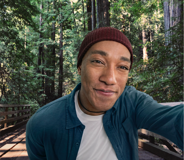 Mixed ethnicity male in hat taking a selfie in front of a wooded forest, not actual Serostim® patient